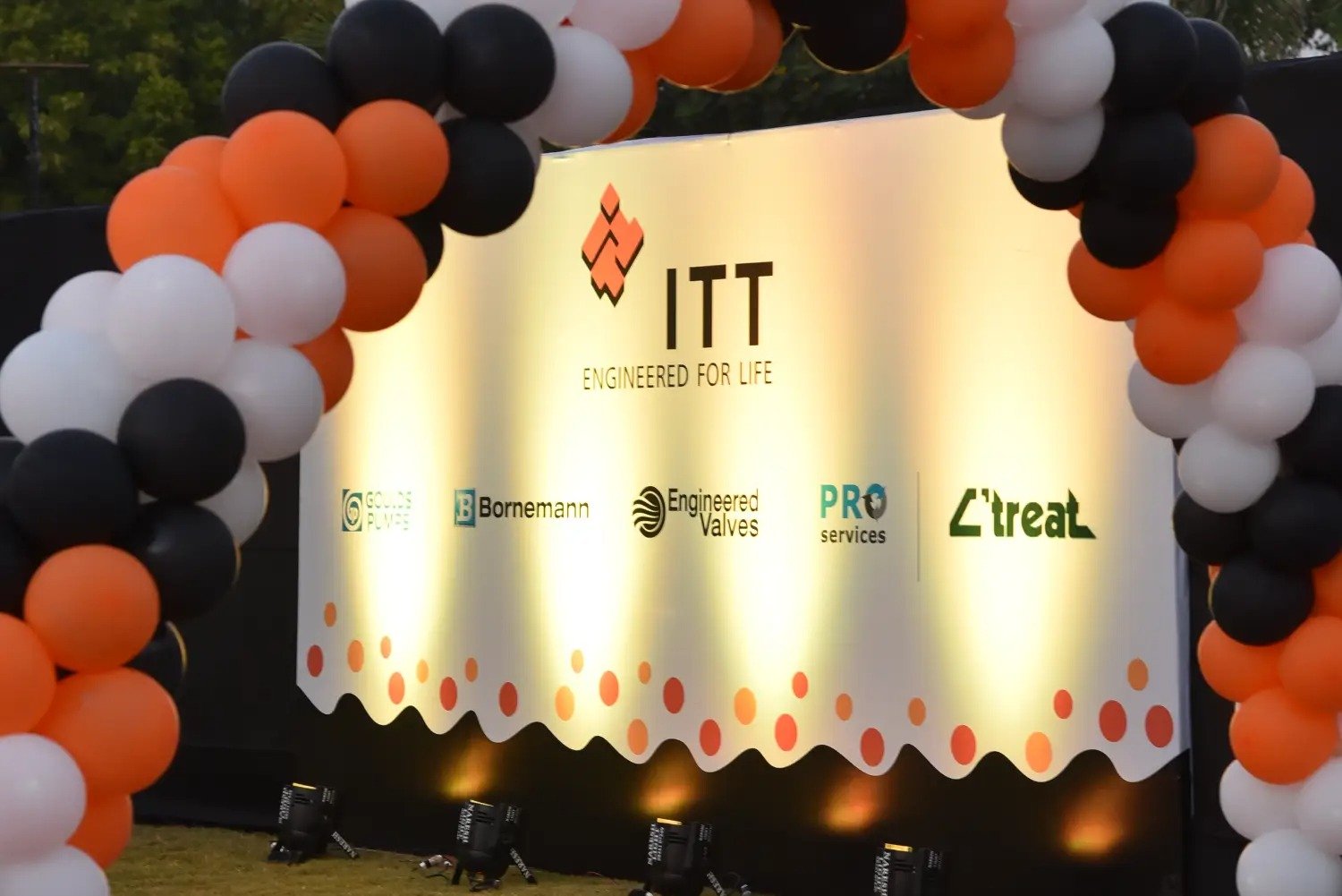 Balloon arch in orange, black, and white colors framing an ITT logo board lit with warm lights